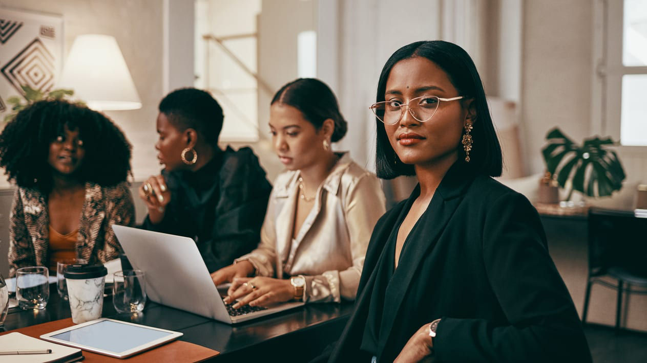 A group of business women sitting around a table with laptops.