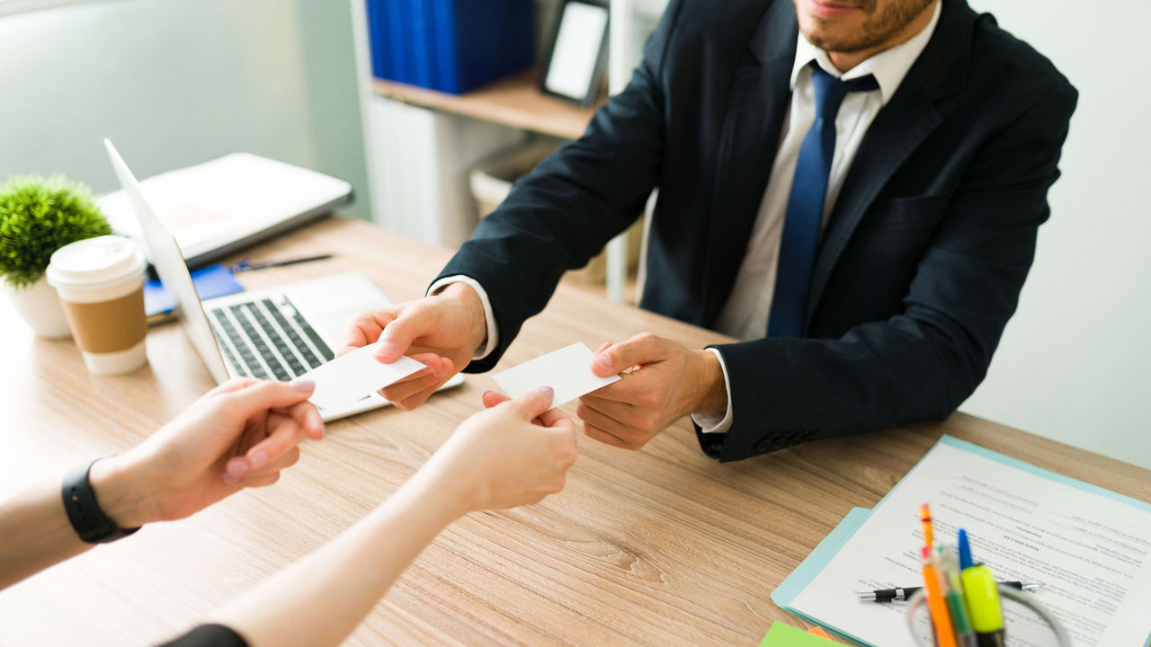 A businessman handing a business card to a woman in an office.