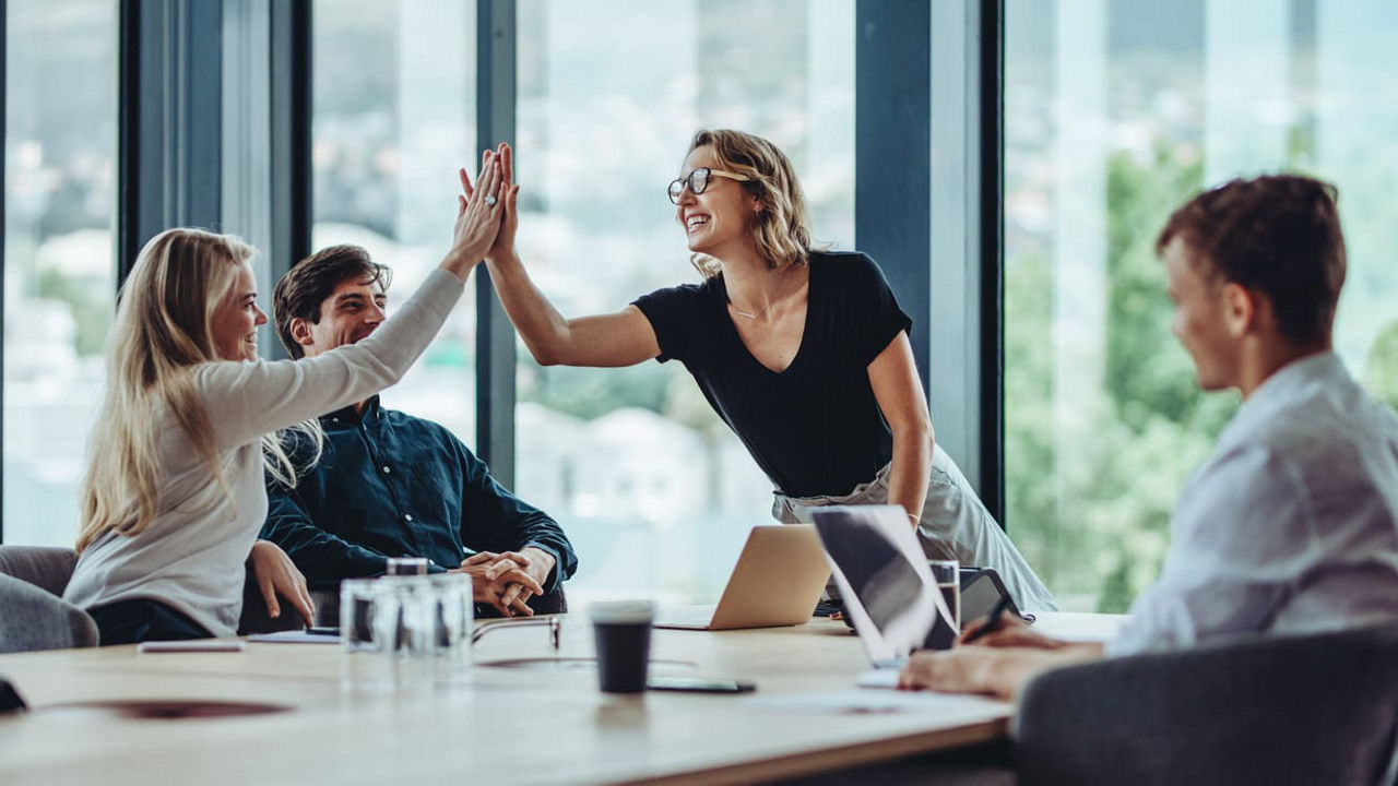 A group of business people giving each other high fives in a meeting.