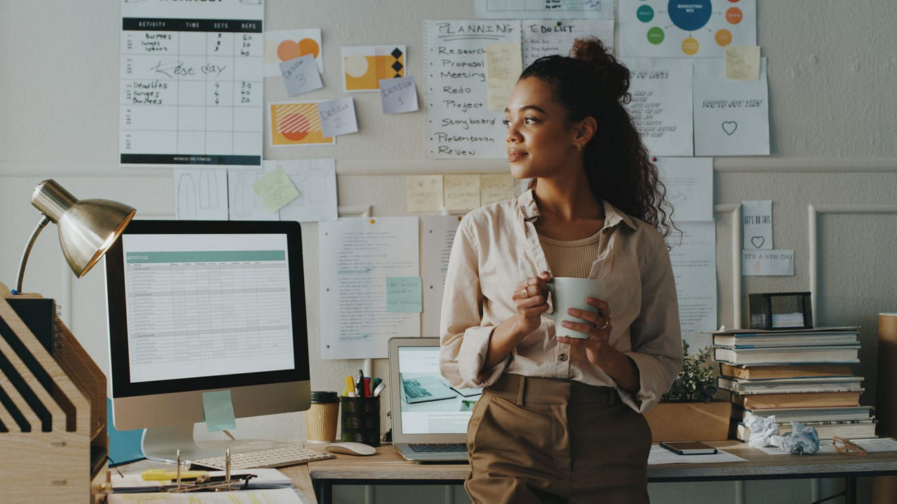 A woman standing in front of a desk with a cup of coffee.