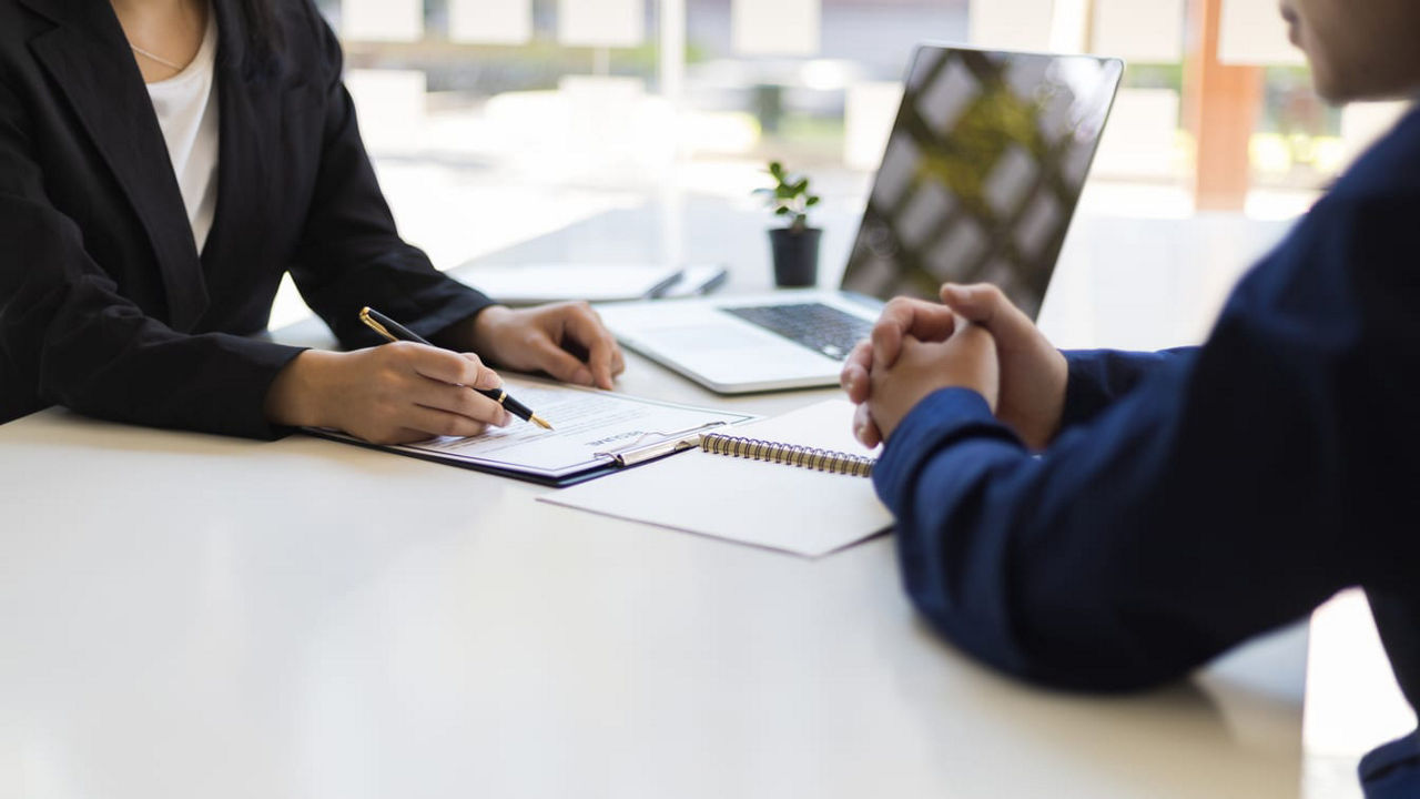 Two people sitting at a desk talking to each other.