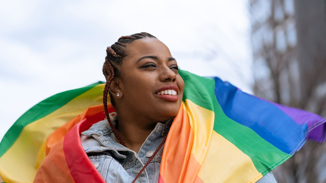 A woman holding a rainbow flag in front of a city.