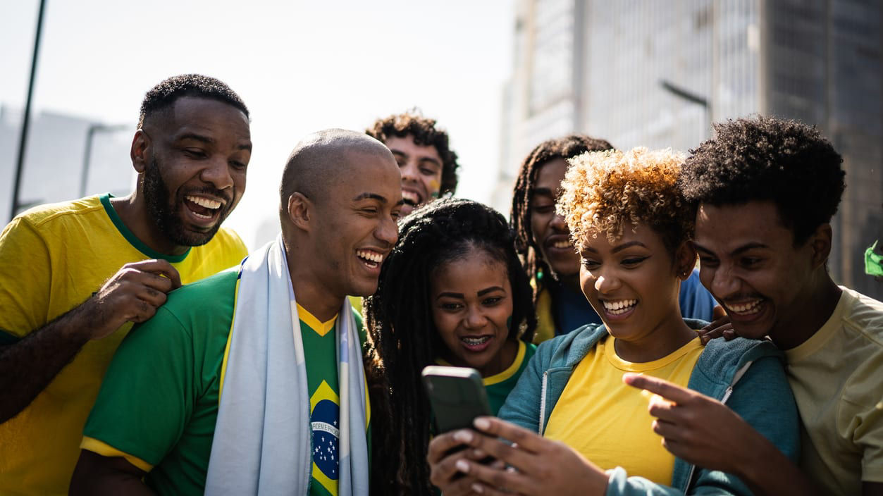 A group of friends smiling huddled together looking at something on a phone.