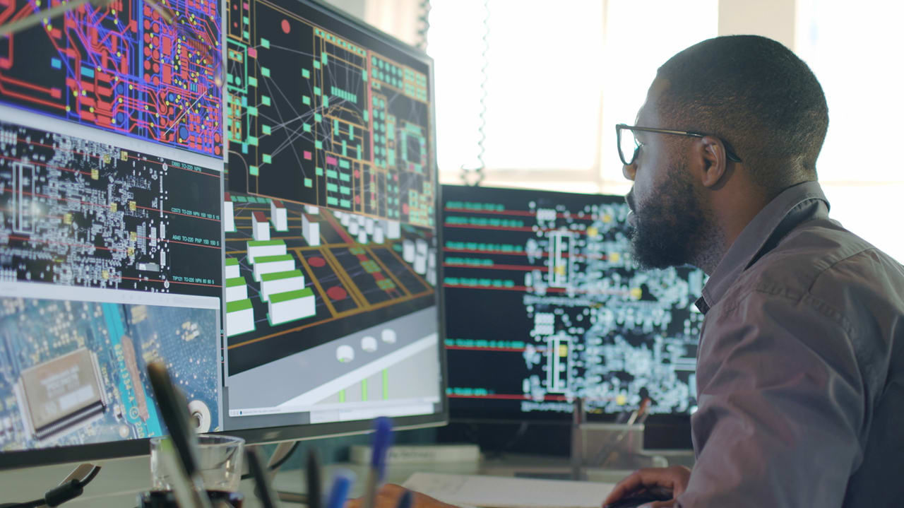 A man sitting in front of several computer screens.