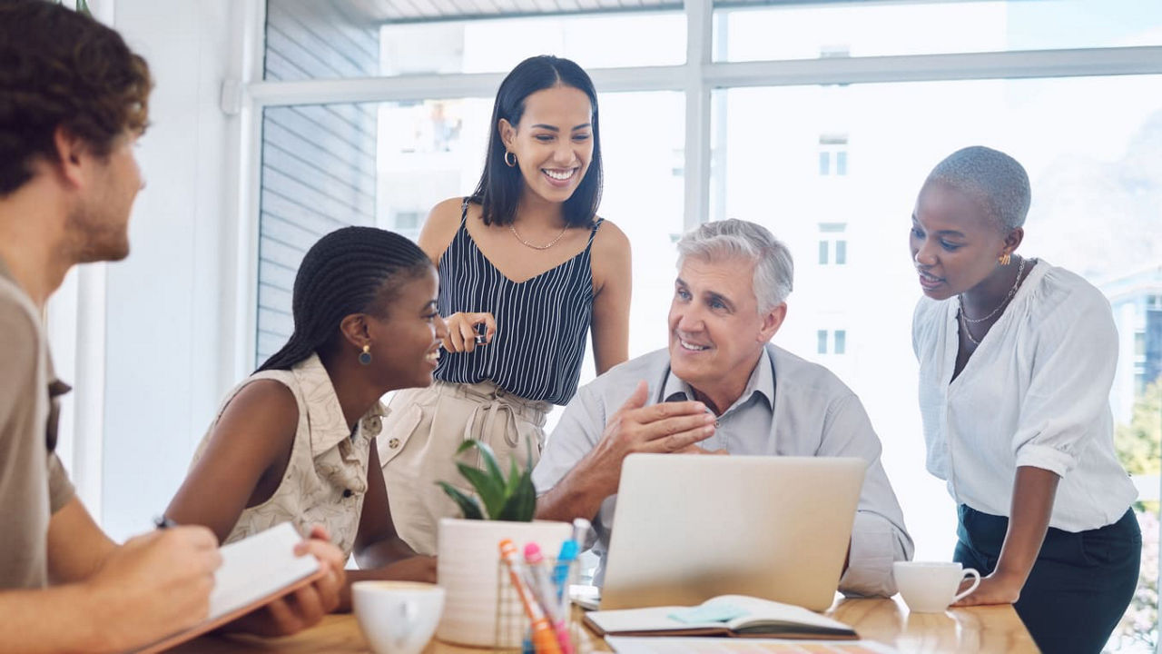 A group of people sitting around a table looking at a laptop.