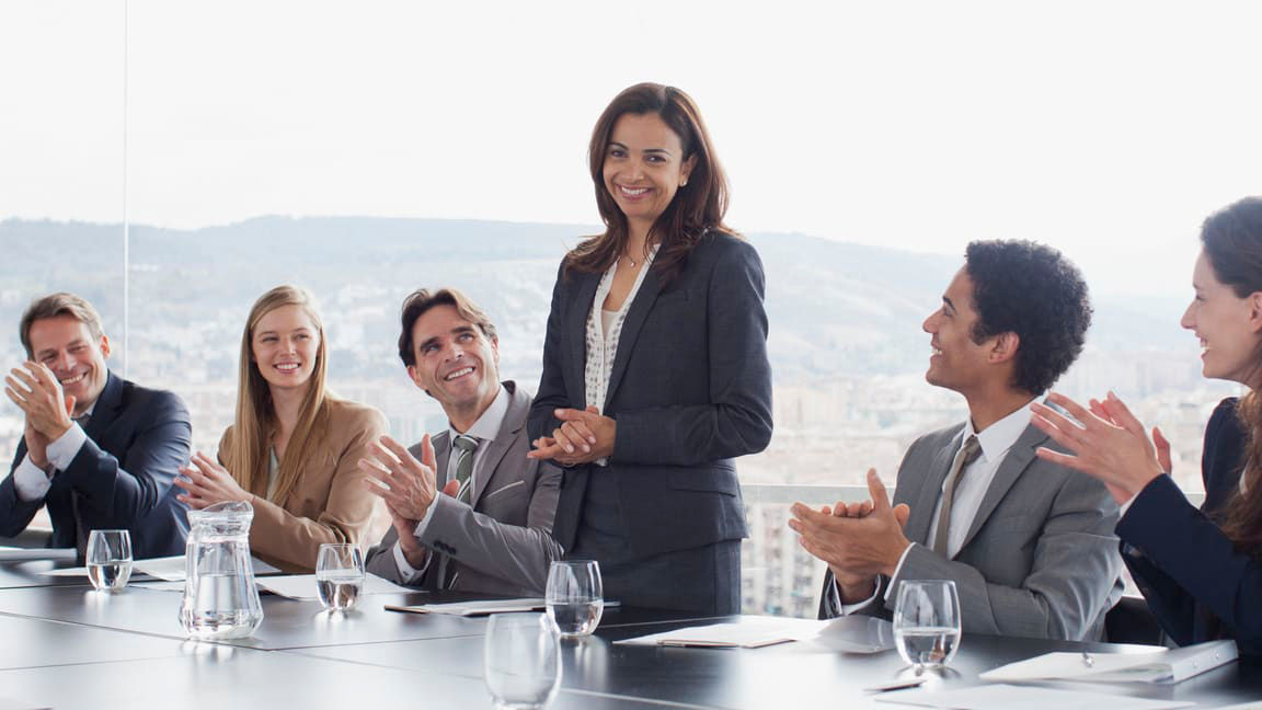 A group of business people clapping at a conference table.