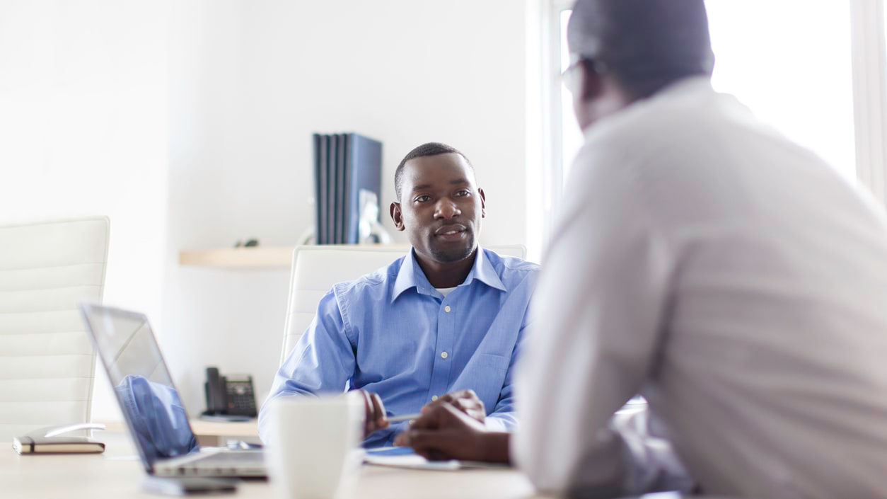 Two business men talking at a table in an office.