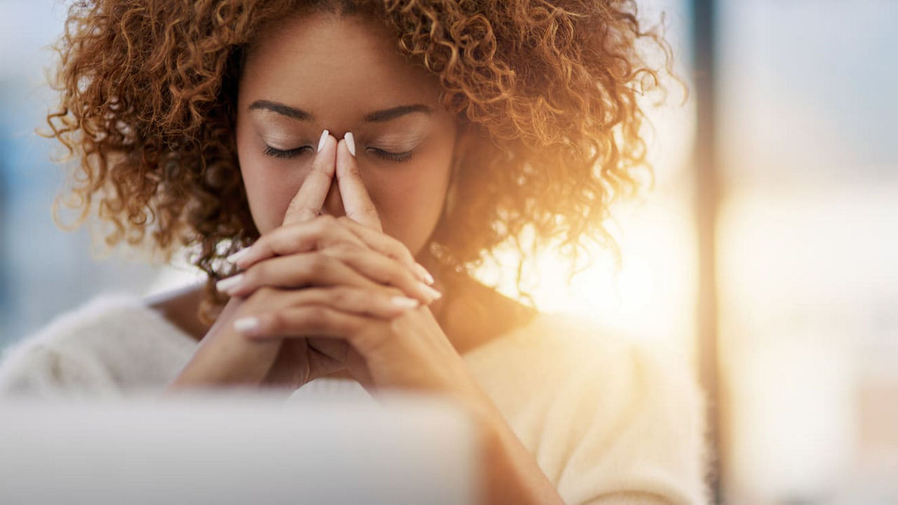 A woman covering her face with her hands while working on a laptop.