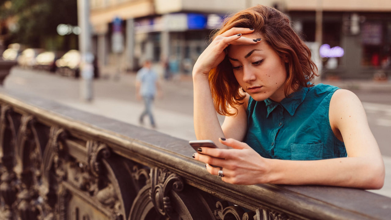 A woman is looking at her phone while sitting on a railing.