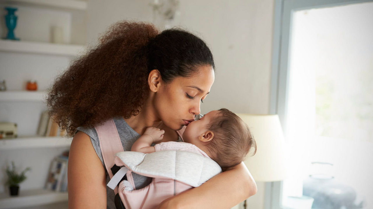A woman kissing her baby in a pink sling.