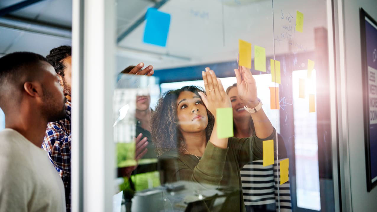 A group of people looking at sticky notes on a glass wall.