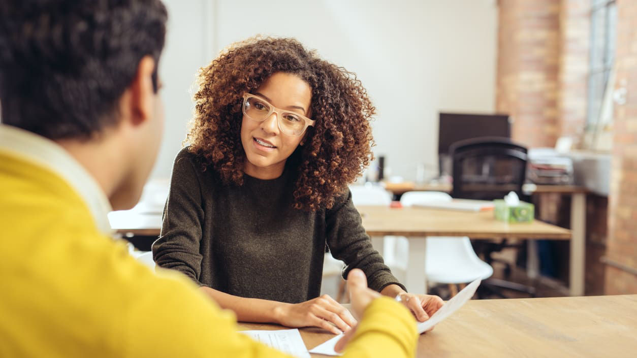 A woman and man talking at a desk in an office.