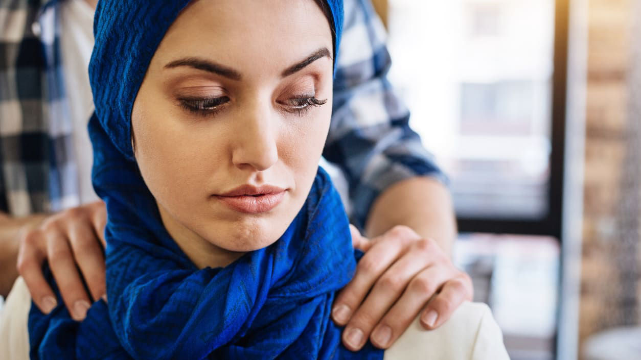 A woman wearing a hijab's shoulders are being massaged by a man.