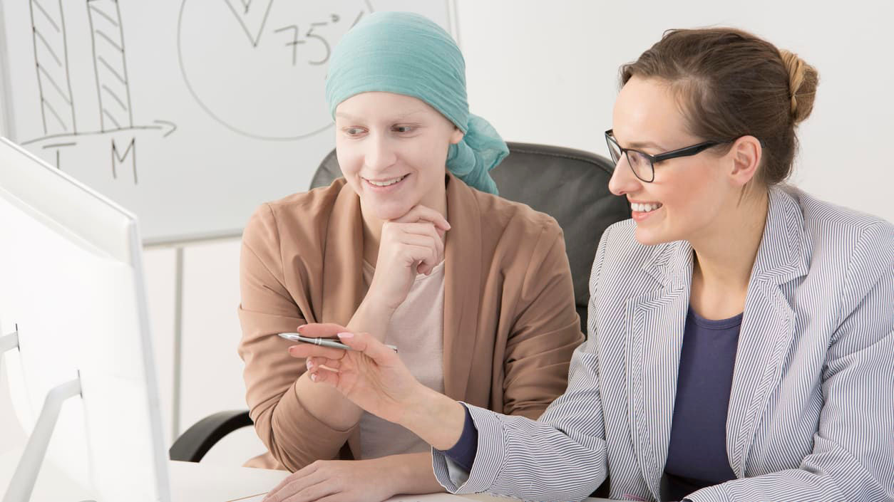 Two women sitting at a desk looking at a computer.