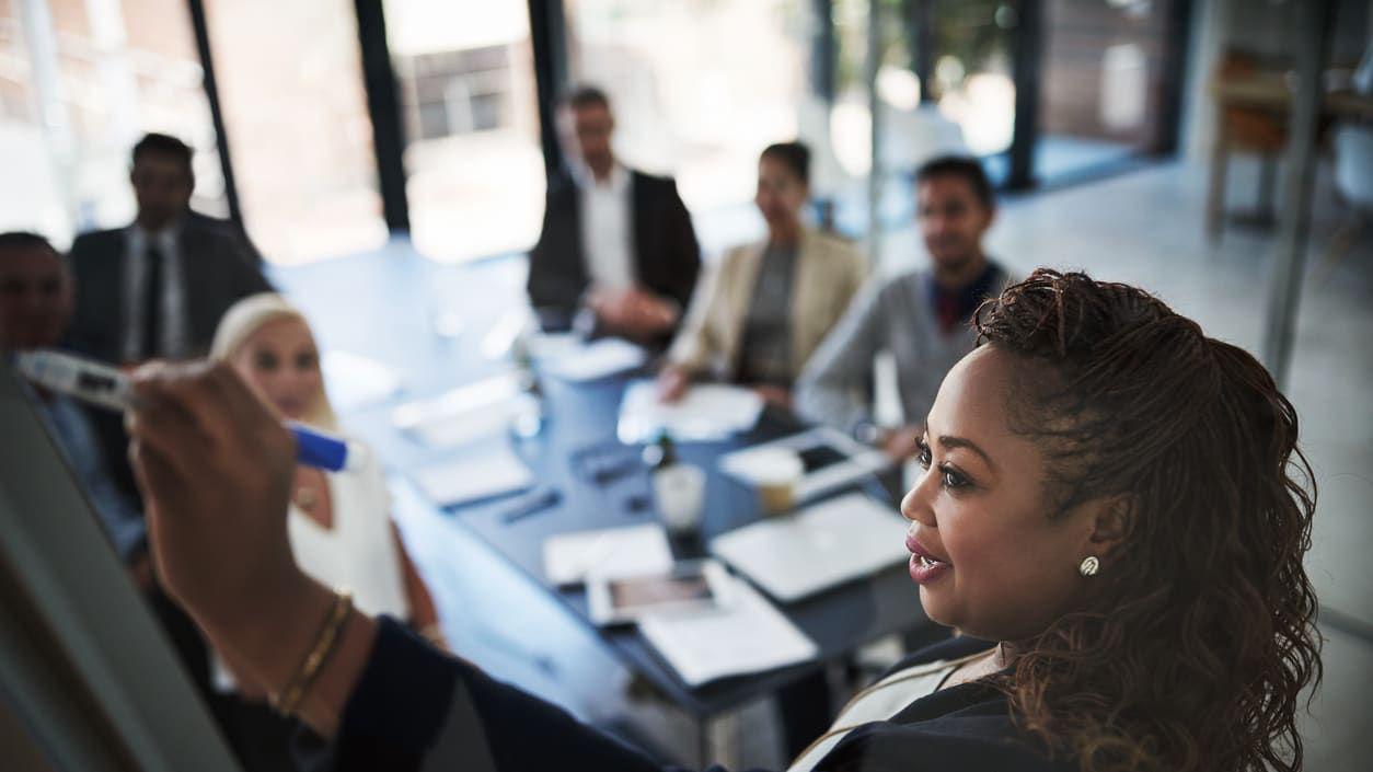 A woman is writing on a whiteboard in a business meeting.