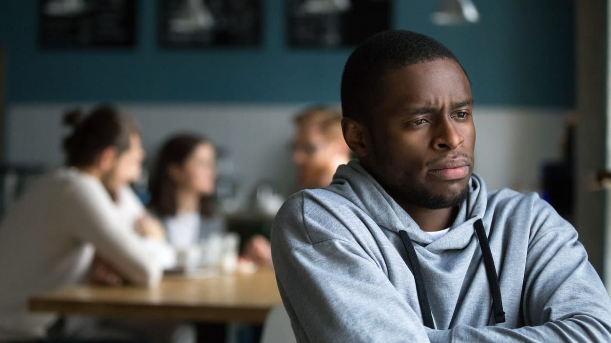 A man sitting in a restaurant by himself looking upset.