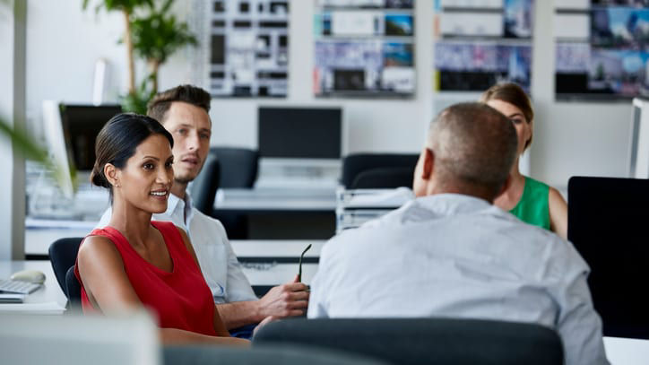 A group of people sitting at a desk in an office.