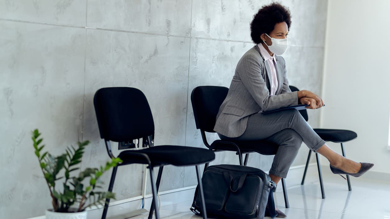 A woman wearing a face mask sitting in a waiting room.
