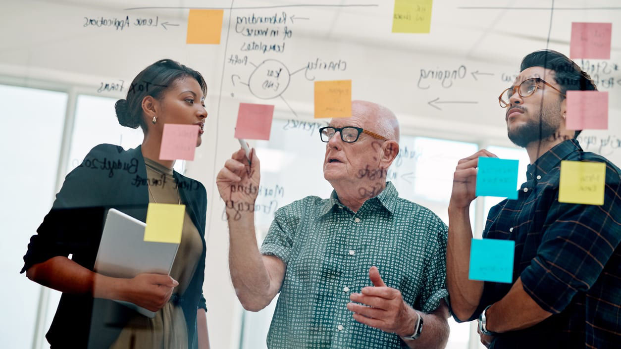 A group of people looking at sticky notes on a glass wall.