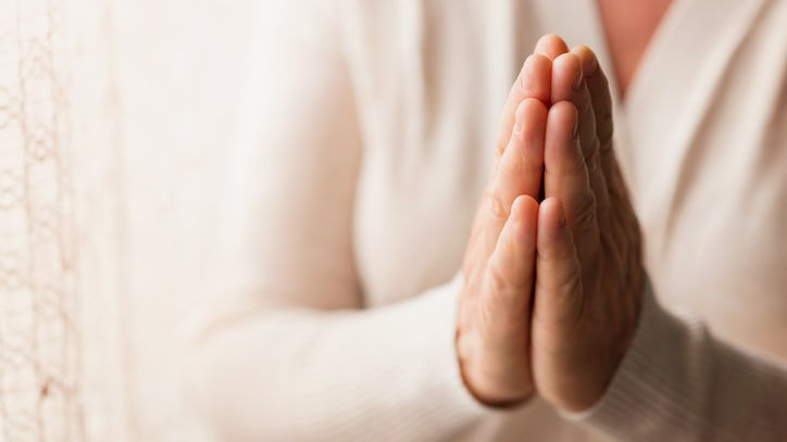 A woman is praying in front of a window.