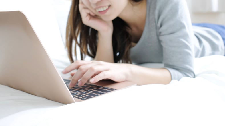 A woman laying on a bed with a laptop on her lap.