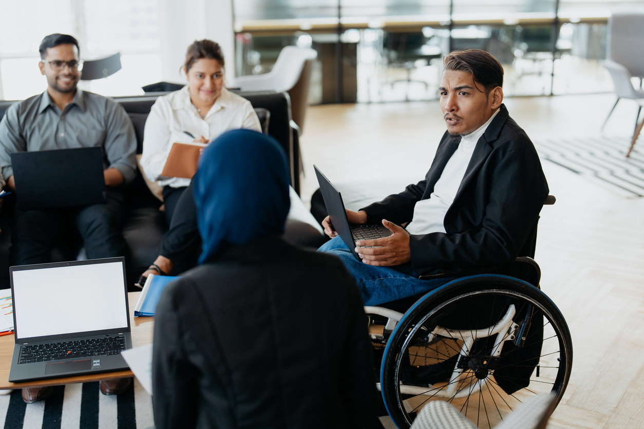 An Asian disabled businessman on wheelchair explaining business plans to his team during a meeting