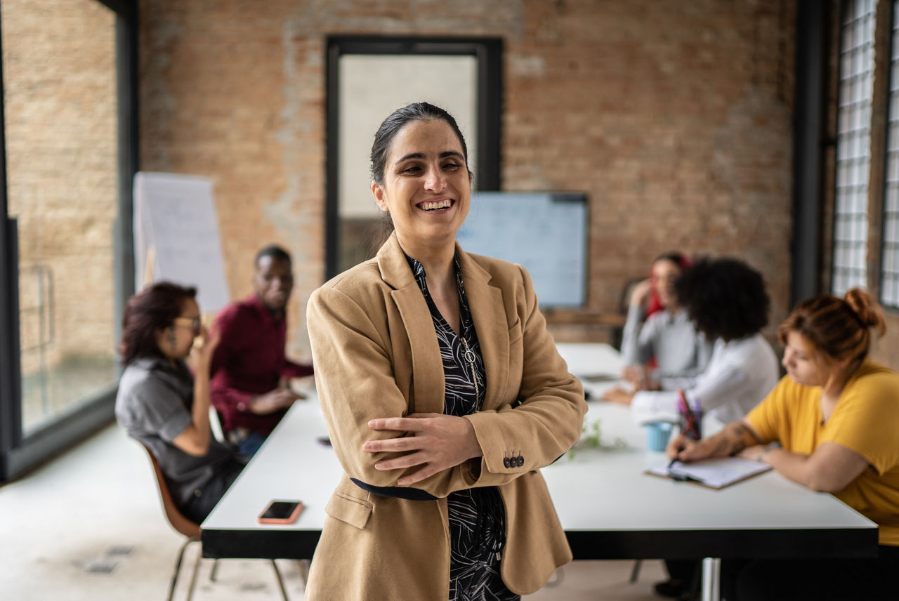 Woman standing in front of a conference table of coworkers smiling at camera