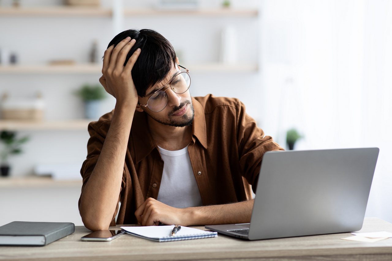 Worried man sits in front of laptop in office. 