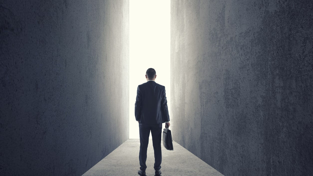 A man in a suit is standing in a dark hallway.