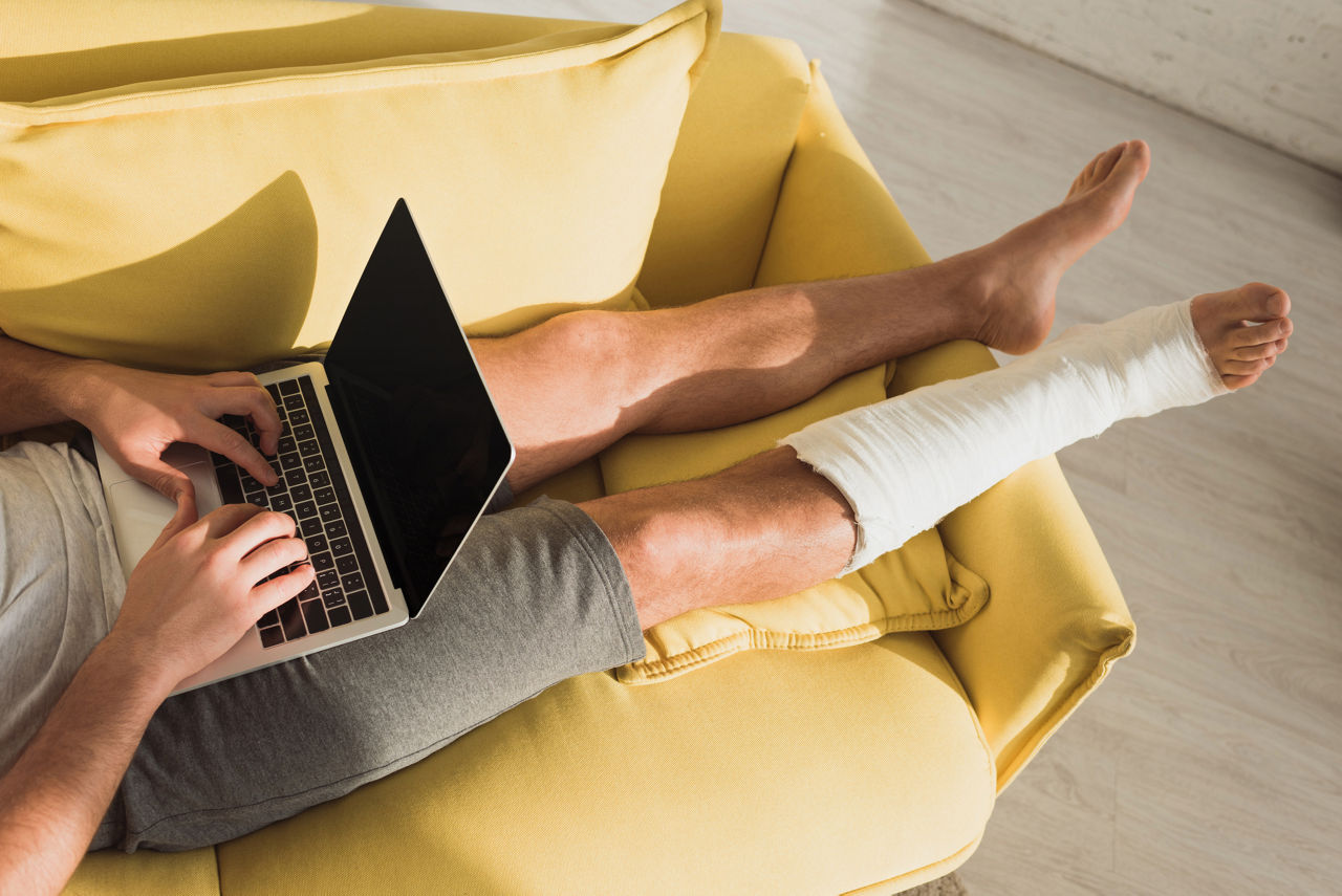 Cropped view of a person with leg in plaster bandage using laptop on sofa at home