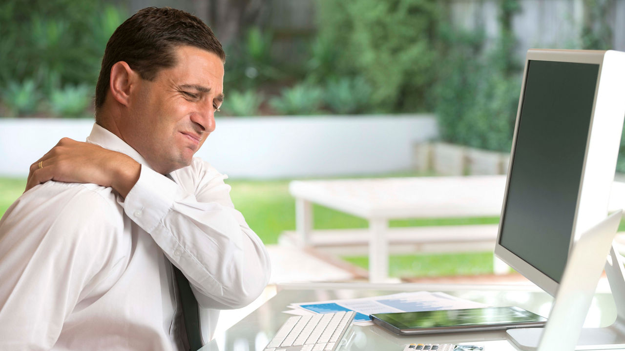 A man sitting at a desk with a pain in his neck.