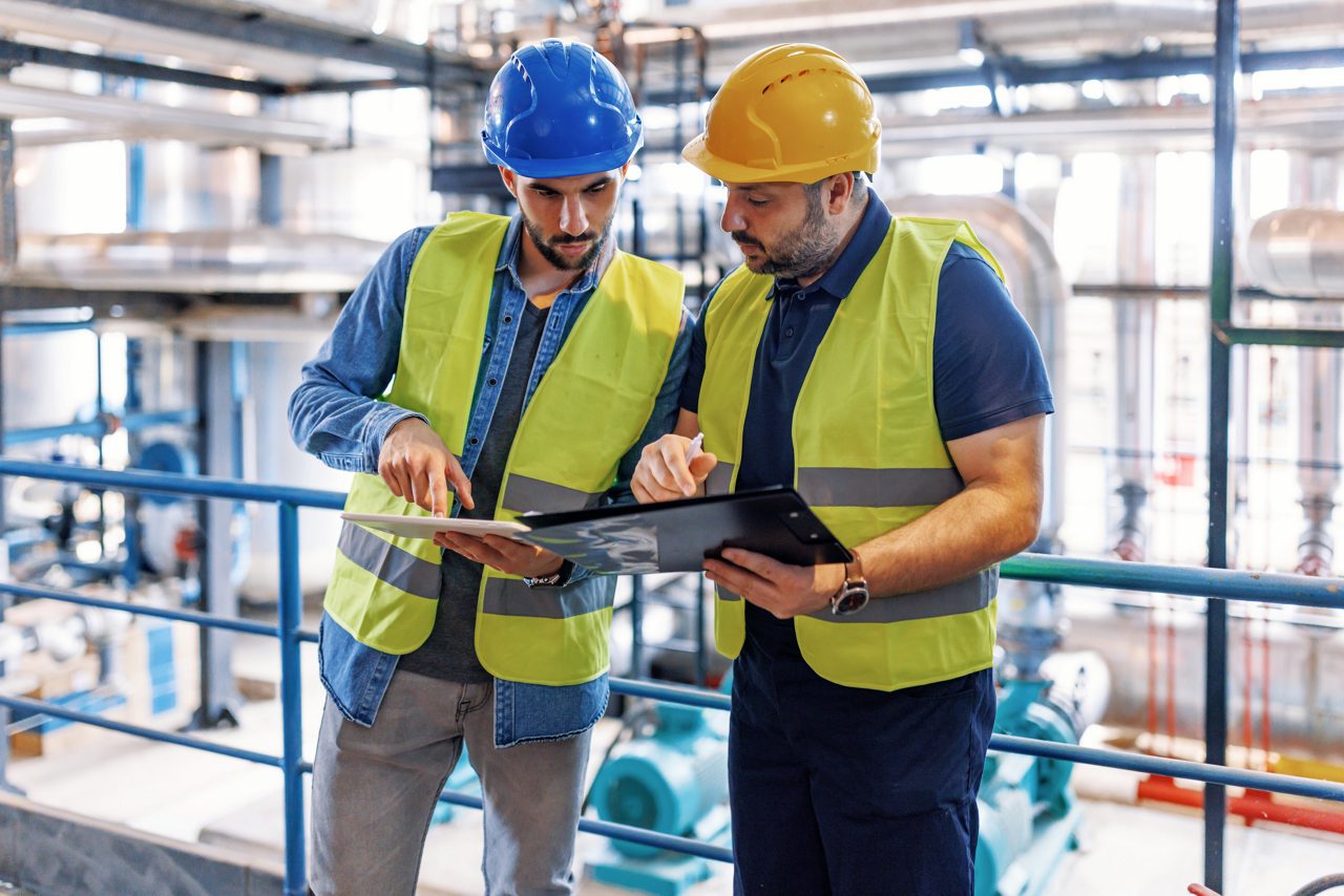 Two inspectors with hard hats and safety vests on, holding clipboards