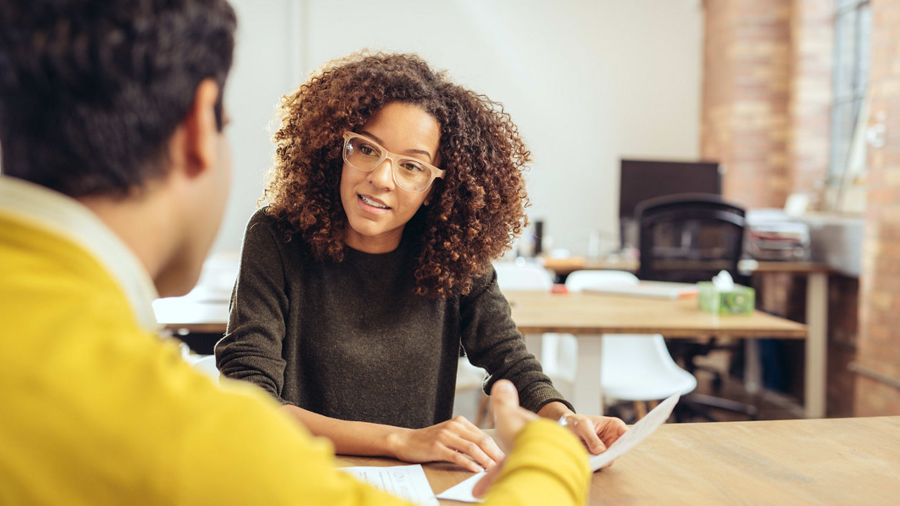 A woman and man talking at a desk in an office.
