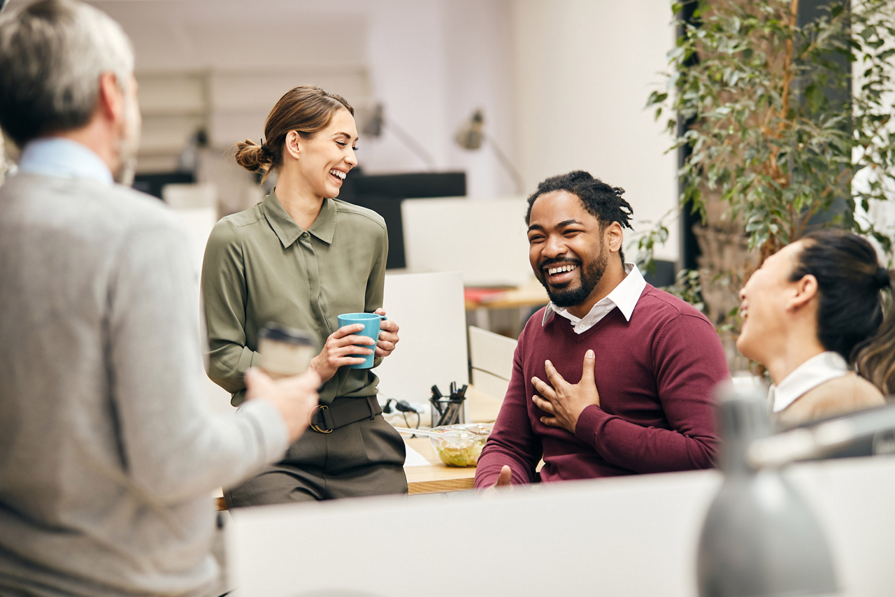 Multi-ethnic group of entrepreneurs laughing while talking to each other on a break in the office.