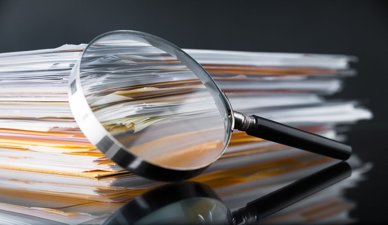 A magnifying glass on a stack of business documents.