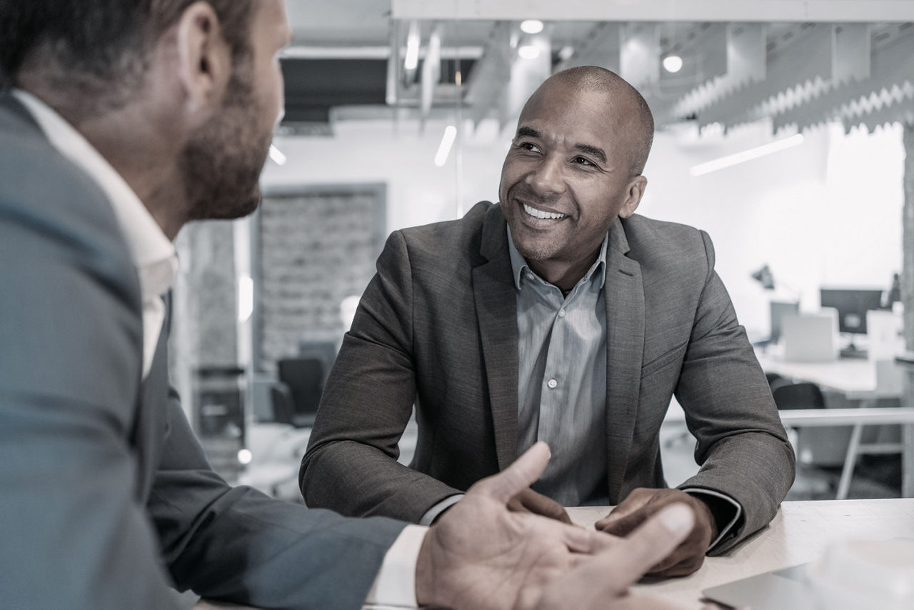 Two men speaking at a table. They are leaning toward each other and demonstrating interest, exemplifying positive body language. 
