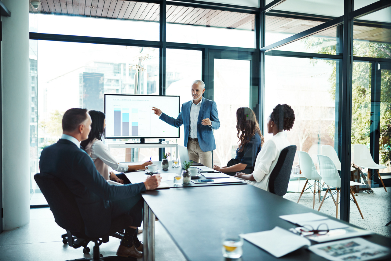A team meeting in a modern conference room with a man presenting charts on a screen. 