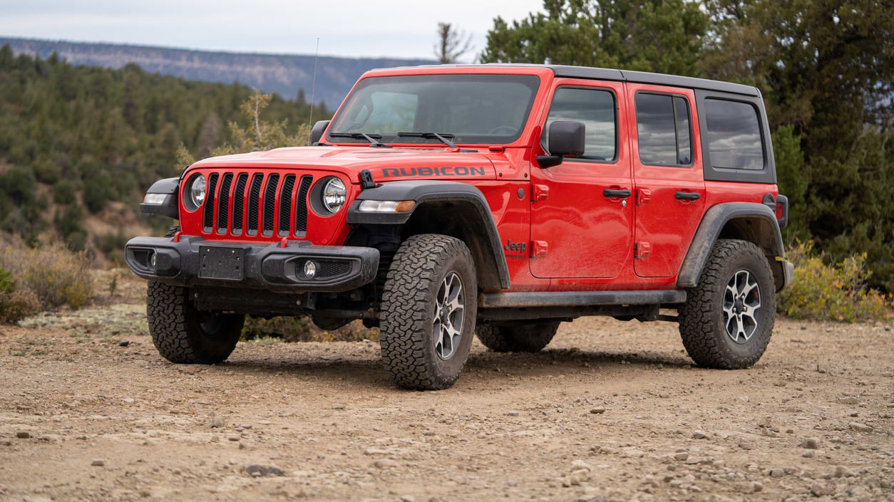 The red jeep wrangler is parked on a dirt road.