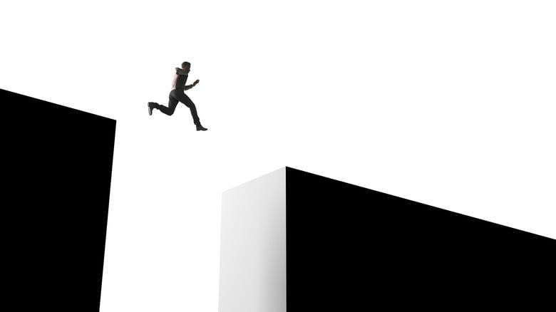 A black and white image of a man jumping over a cliff.