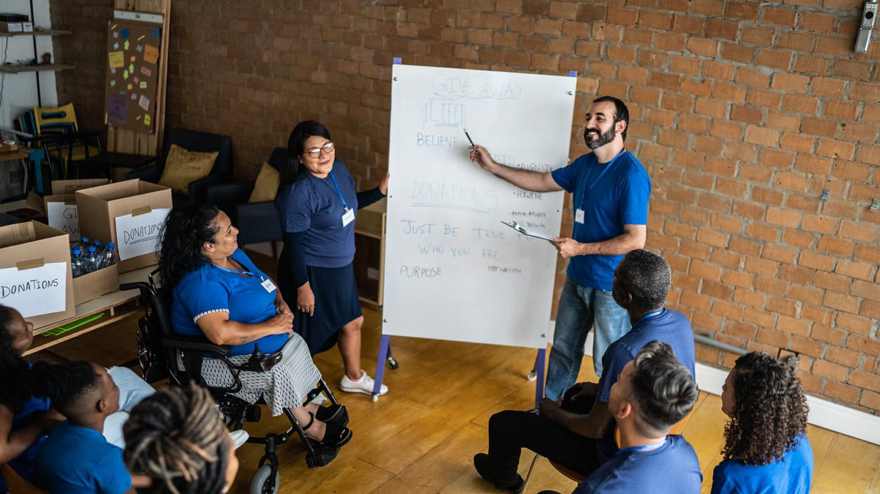 A group of people in blue shirts are sitting around a white board.