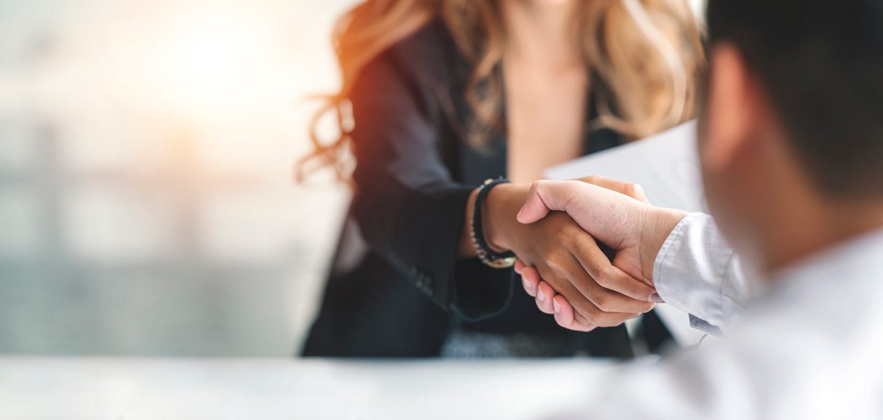 People shaking hands in an office, symbolizing a deal or job acceptance