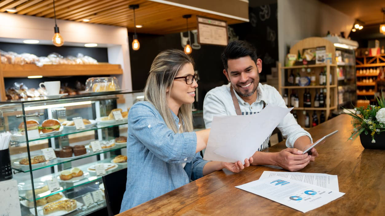 A man and woman working at the counter of a bakery.