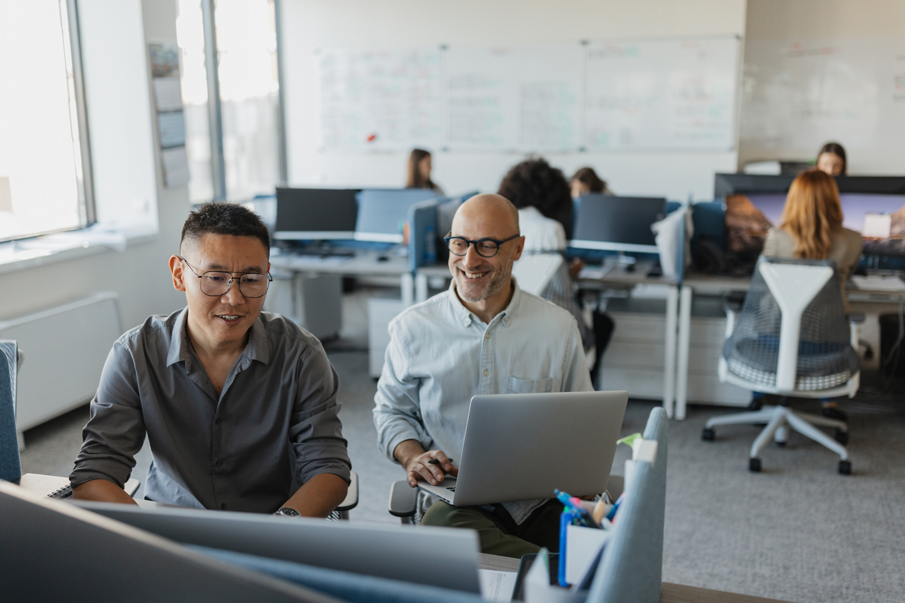 Two male colleagues share insights and collaborate together over a laptop, highlighting teamwork and the exchange of ideas in a dynamic office setting.