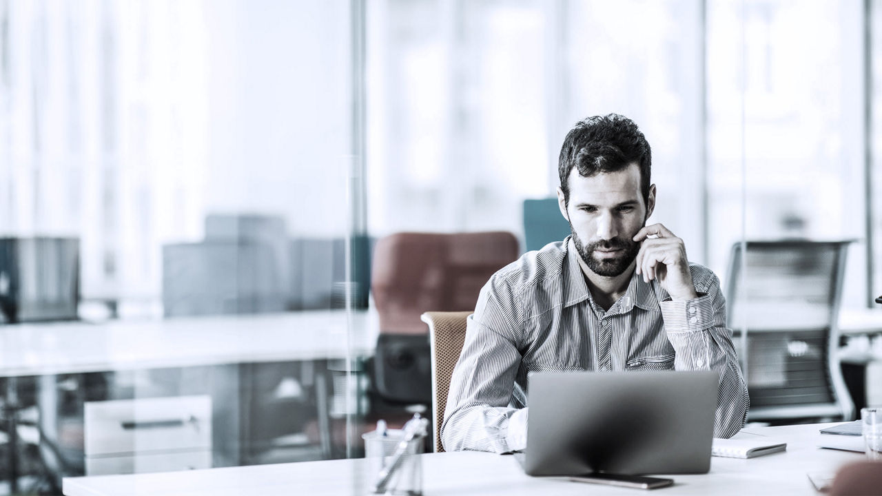 A man is talking on the phone while sitting at a desk in an office.