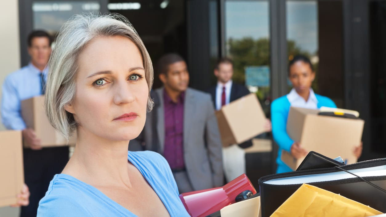 Laid-off workers leaving an office building carrying boxes of personal items.