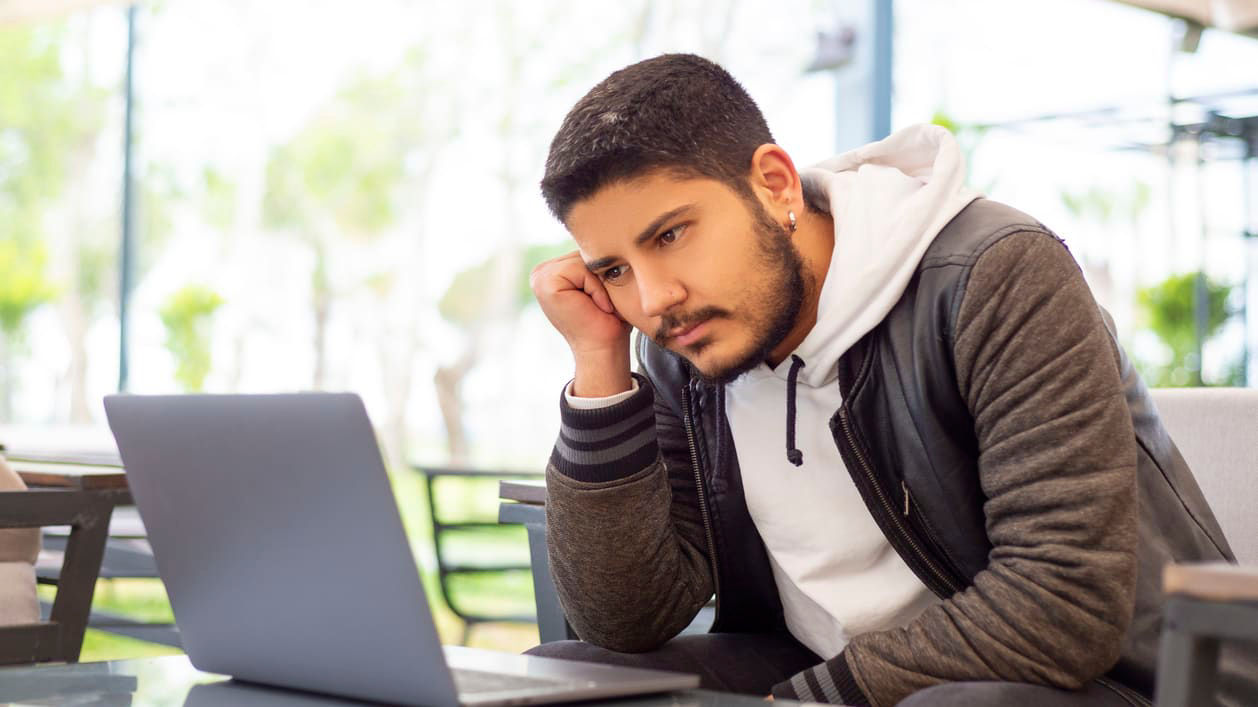 A man sitting at a table looking at his laptop.