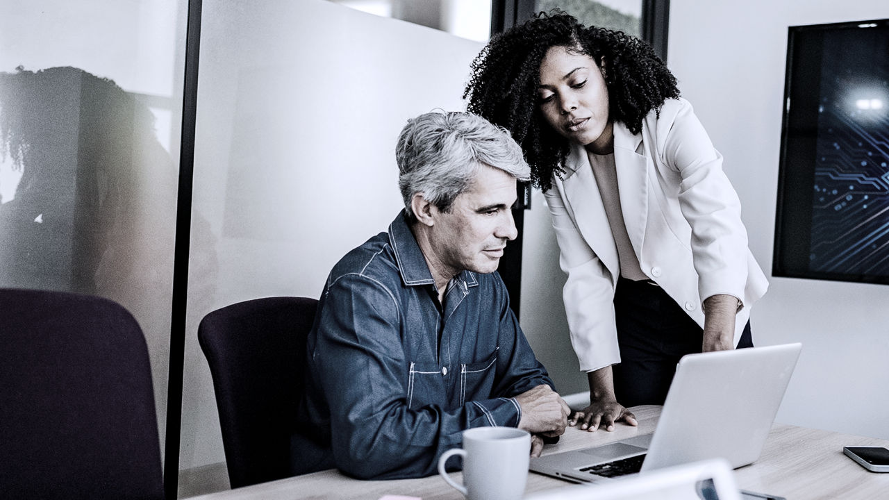 Female leader training manager, who is sitting at table looking at laptop
