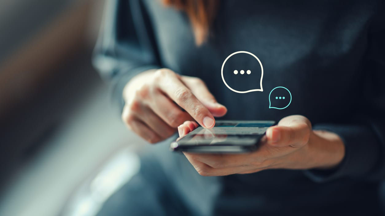 A woman is using a smartphone with a chat bubble on it.