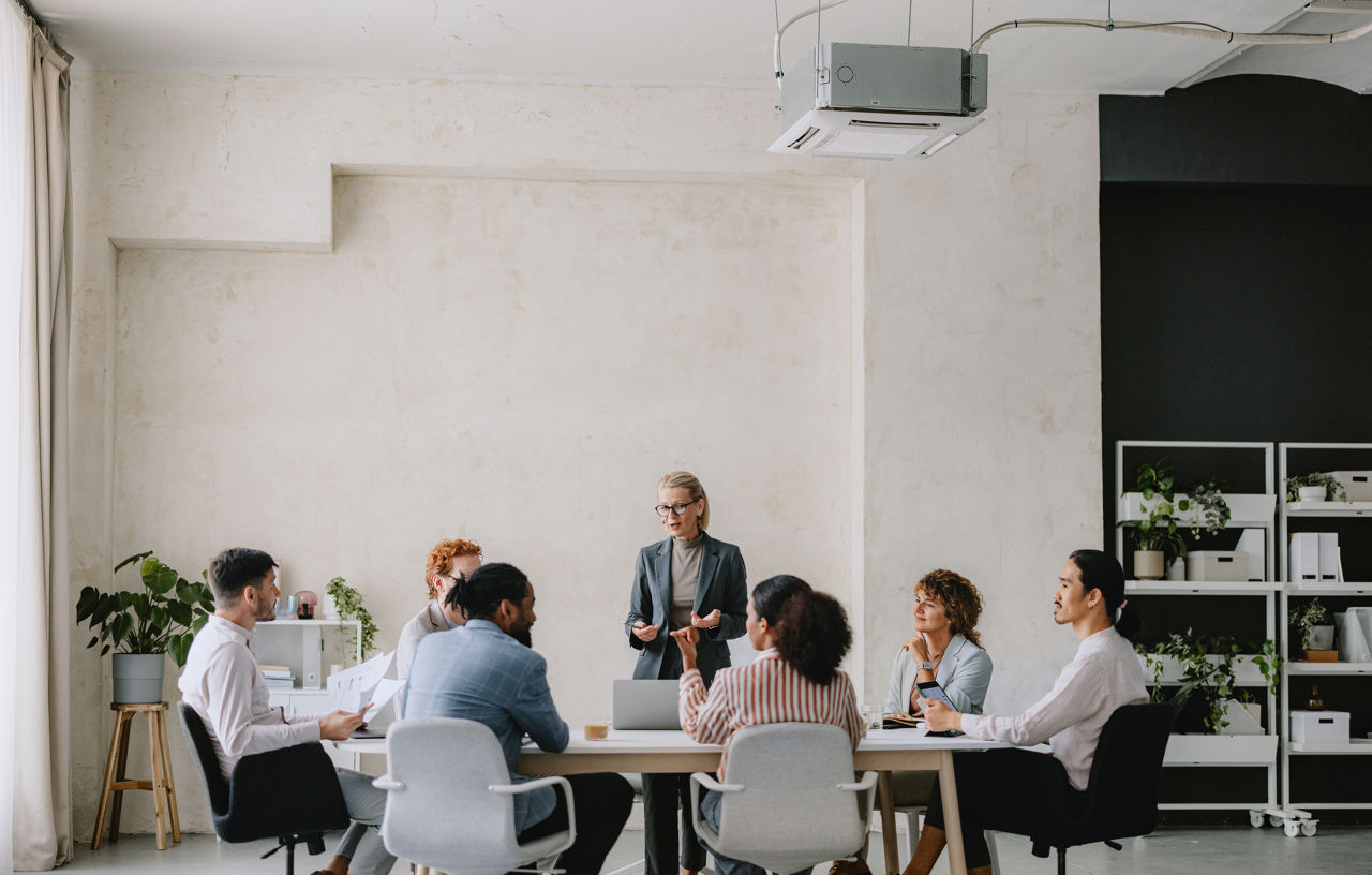 A diverse group of professionals having a business meeting in a bright beige office setting, focusing on collaboration and teamwork.