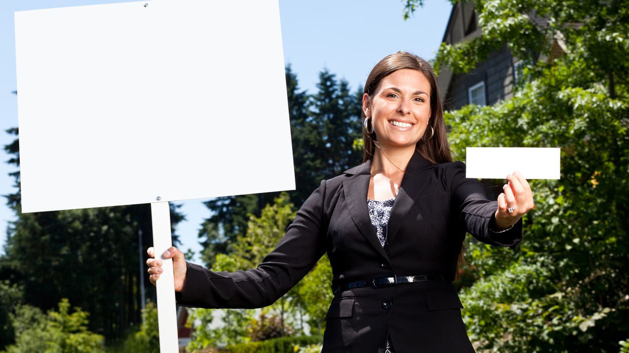 A woman holding up a blank sign in front of a house.